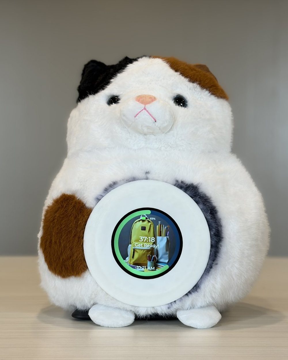 A Merfi plush cat on a desk with its round screen showing a countdown that reads 37:18, 'Get Ready!', and a backpack for the next activity