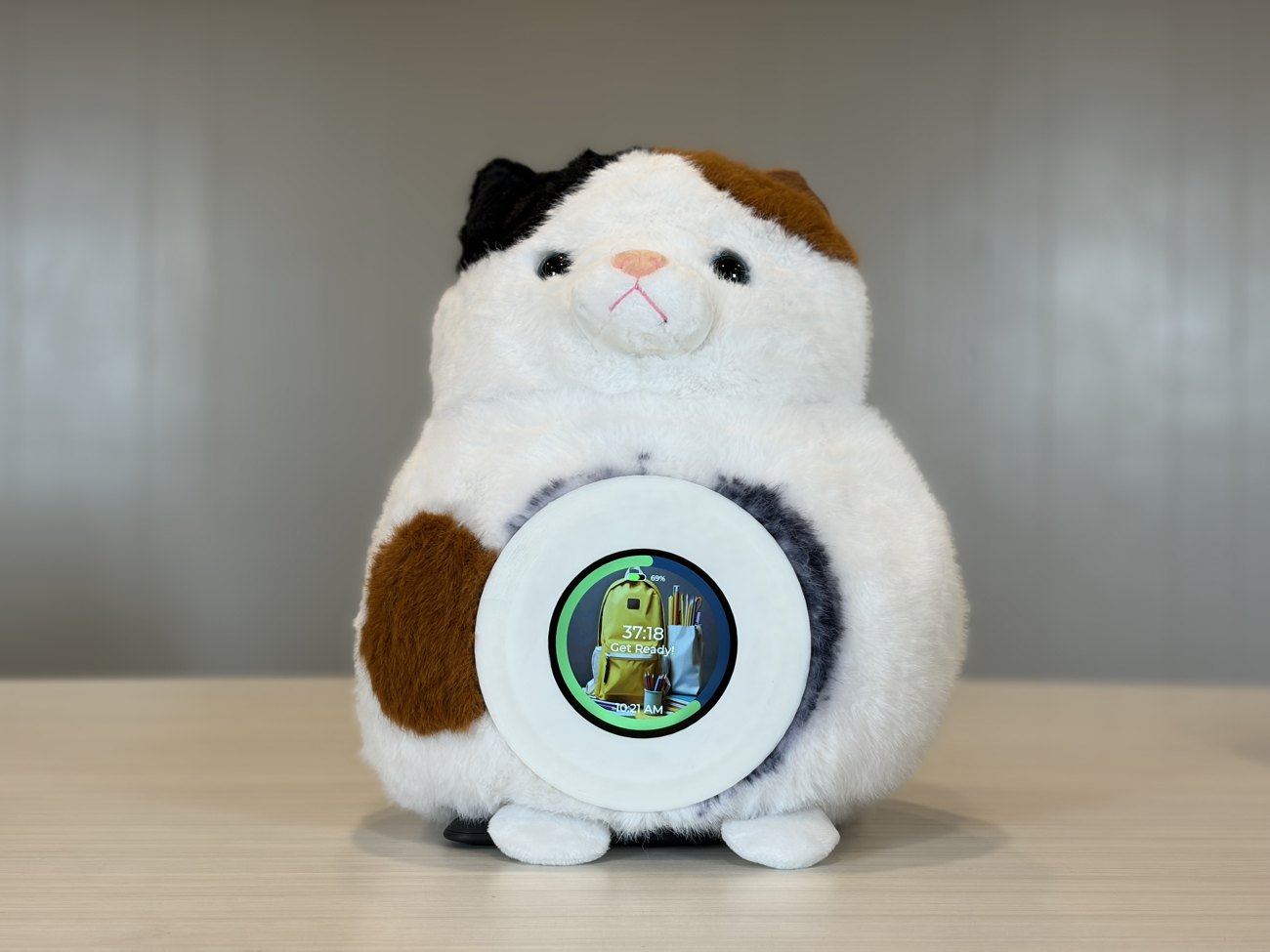 A Merfi plush on a desk with its round screen showing a countdown that reads 37:18, 'Get Ready!', and a backpack for the next activity
